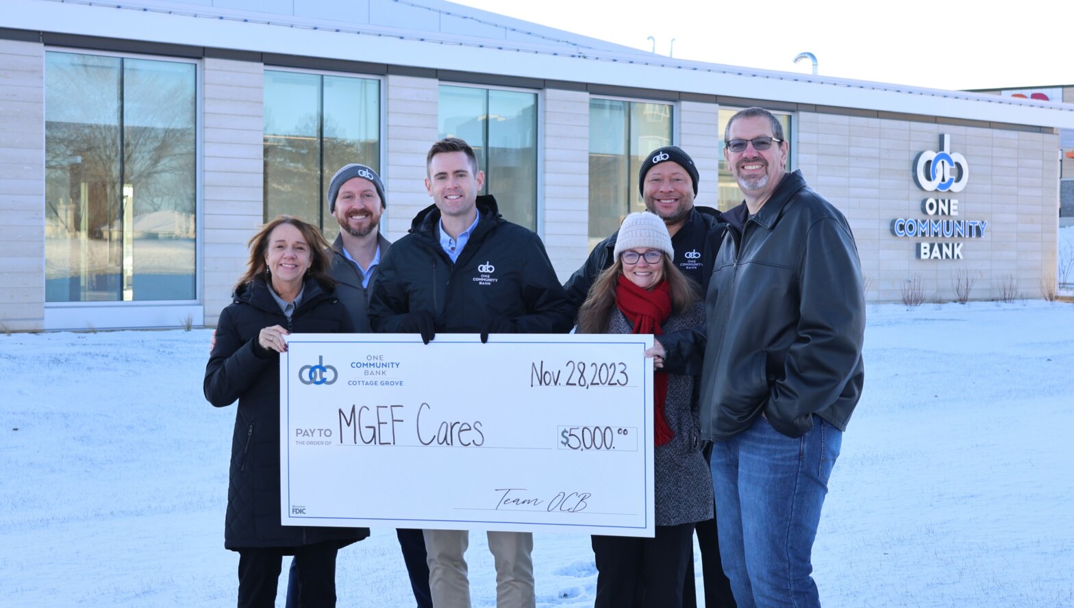 OCB colleagues present a $5,000 big check donation to the Monona Grove Education Foundation's President for their CARES Campaign in front of OCB's new bank location in Cottage Grove.